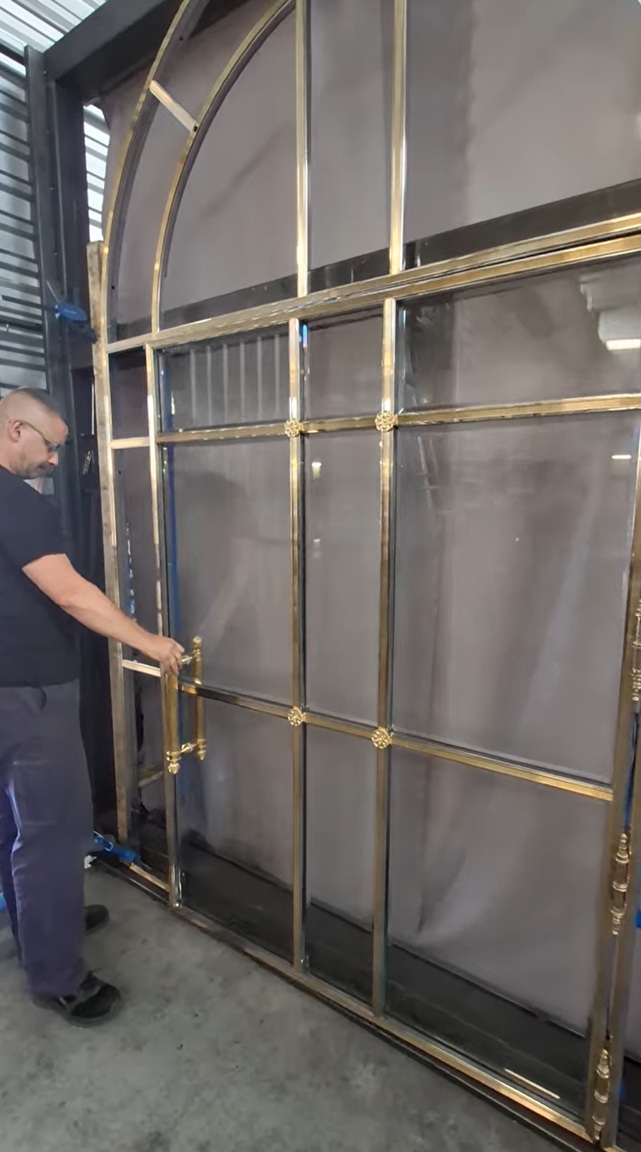 Arched metal door with a grid design, person in black standing beside it.