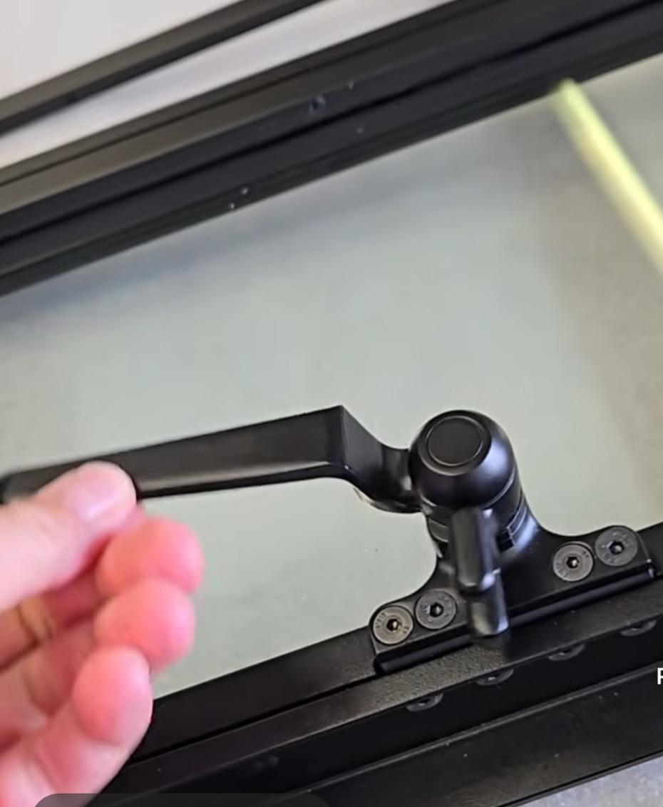 Hand reaching for a black window latch on a glass panel.