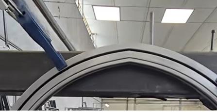 Metal frame with curved top and clamp in a workshop setting.