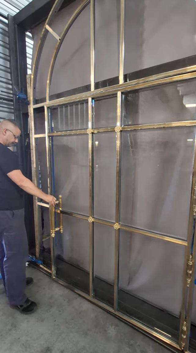 Arched metal door with a grid design, person in black standing beside it.